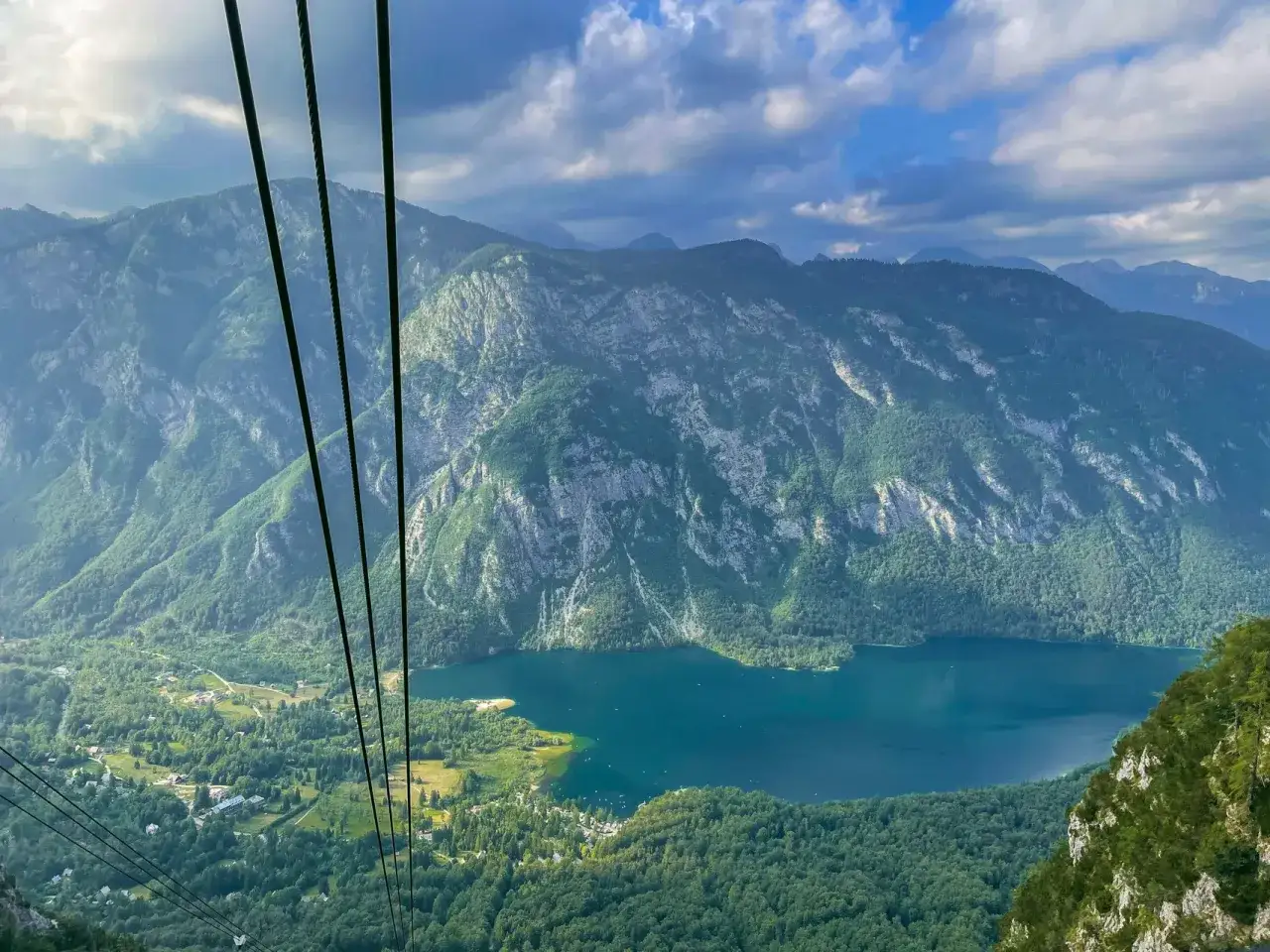 Widok z kolejki linowej na malownicze jezioro Bohinj otoczone zielonymi górami.