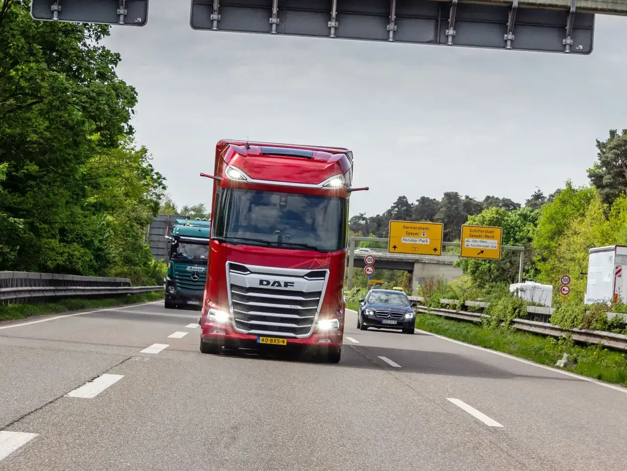 Roter LKW auf Autobahn, der mit hoher Geschwindigkeit f&auml;hrt. Ein gr&uuml;ner LKW und ein Taxi sind ebenfalls zu sehen. Die **Litauen Geschwindigkeit** ist hier ein wichtiges Thema.