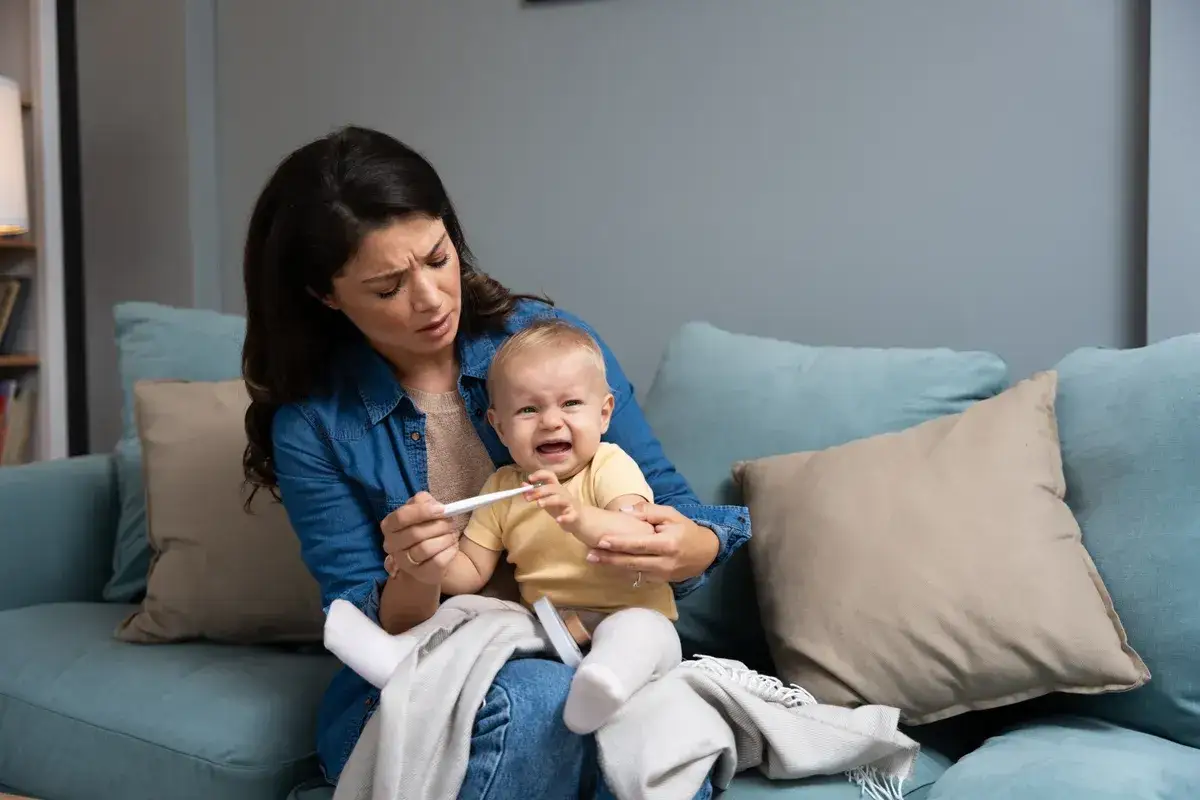 Zmartwiona mama mierzy temperaturę płaczącemu dziecku, które ma gorączkę przy ząbkowaniu.