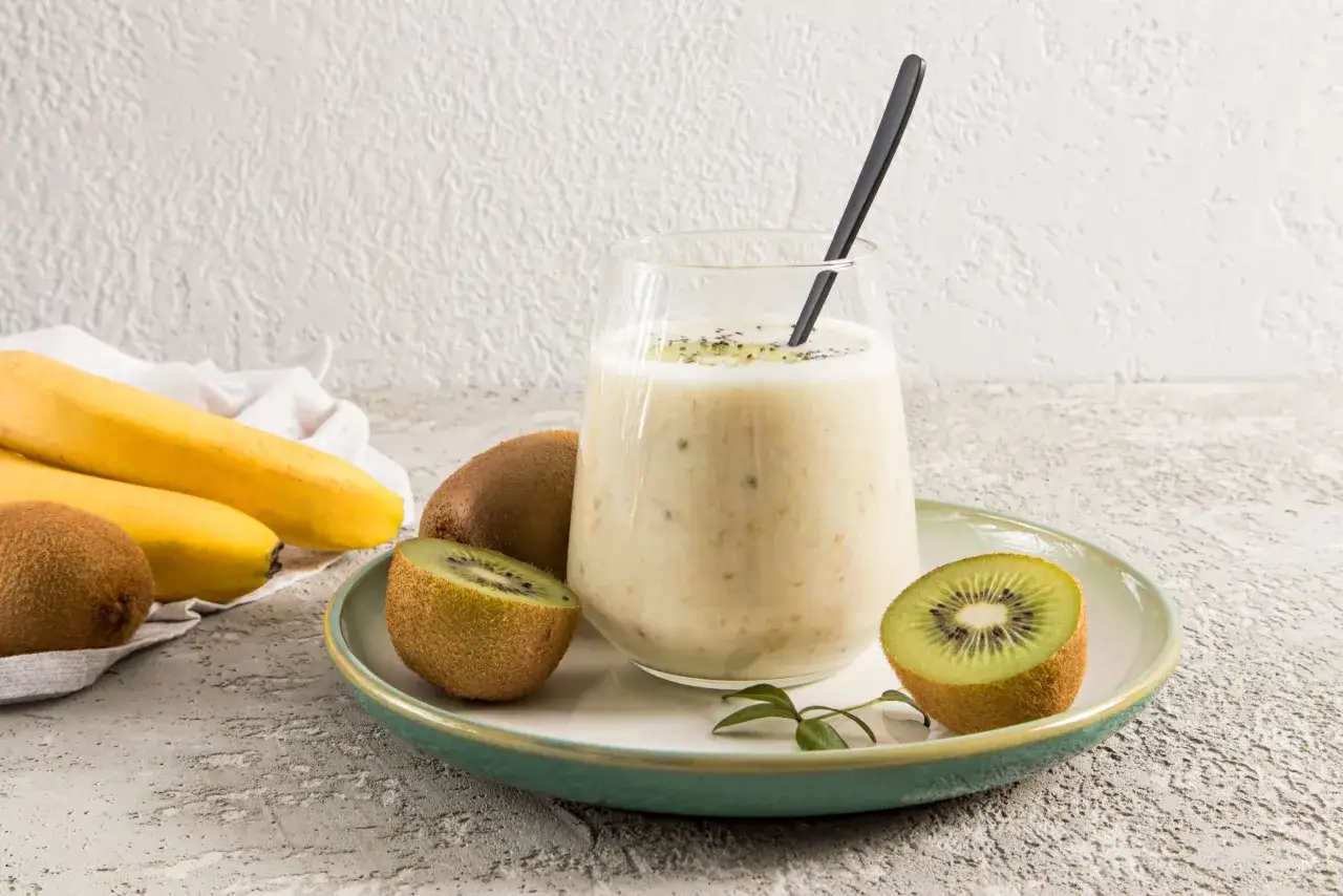 Un verre de smoothie banane kiwi, garni de graines de chia, avec des kiwis et des bananes &agrave; c&ocirc;t&eacute;.