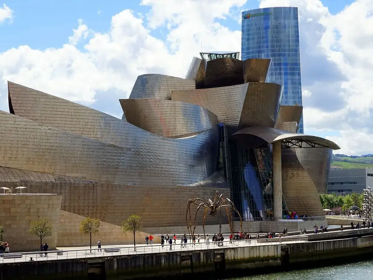 Spektakularny efekt Bilbao: Muzeum Guggenheima w Bilbao, z jego falującymi, metalicznymi formami, przyciąga wzrok. Obok stoi nowoczesny wieżowiec.
