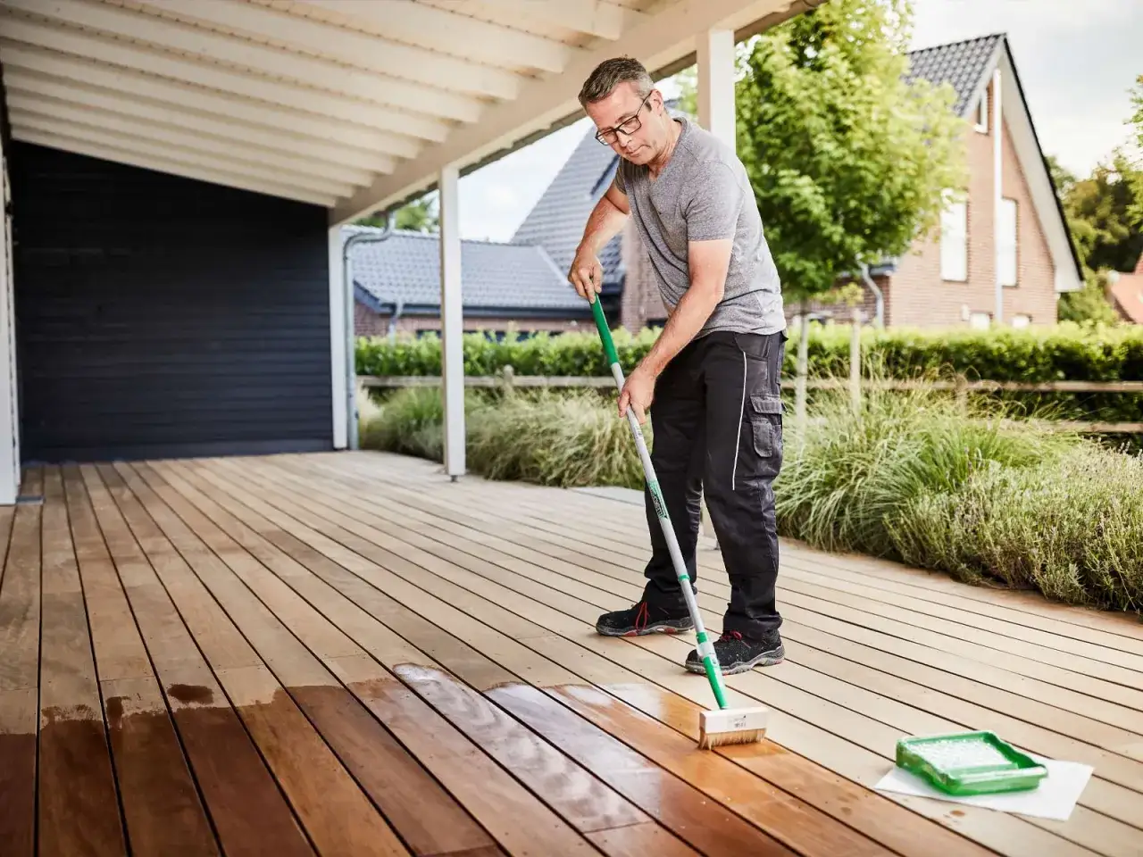 Un homme applique de l'huile sur une terrasse en bois. Il se demande quelle huile pour prot&eacute;ger le bois ext&eacute;rieur.