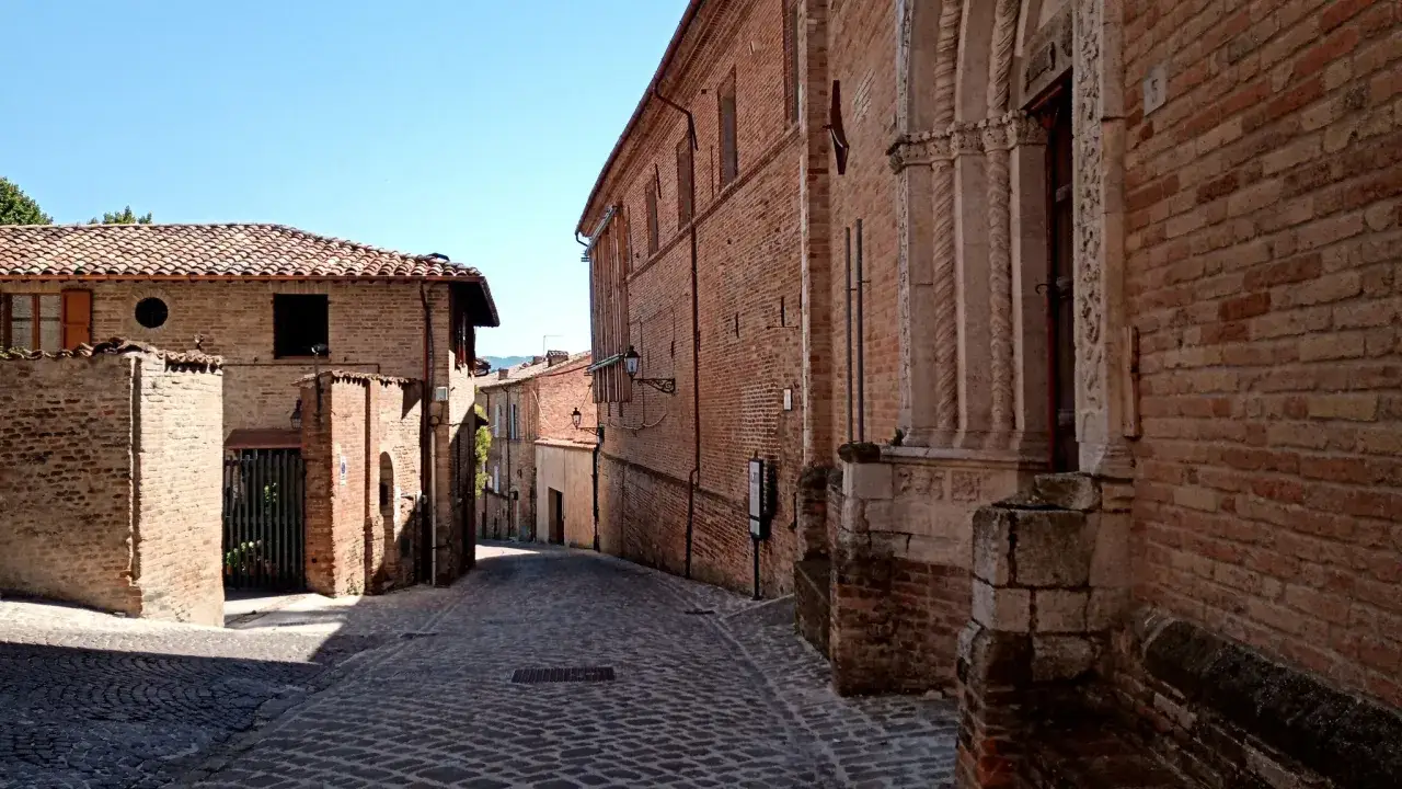 Un vicolo lastricato in Italia, con edifici in mattoni rossi e un portale decorato. Un luogo incantevole da esplorare, amandola cosa vedere.