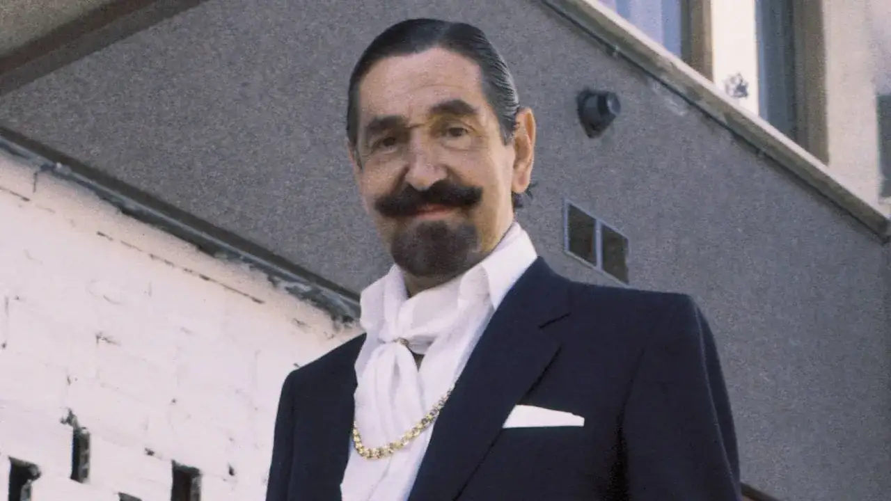 Jaime de Mora y Aragón, con su característico bigote y perilla, luce un traje oscuro, pañuelo blanco y cadena dorada.