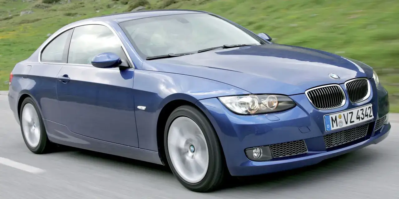 Niebieskie BMW E92 335d w ruchu, z widocznym przodem i bokiem, na tle zielonych wzgórz.
