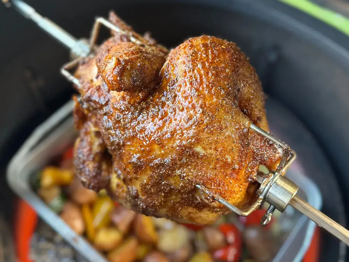 Pollo al horno dorado y jugoso girando en un asador, con papas y pimientos asados debajo.