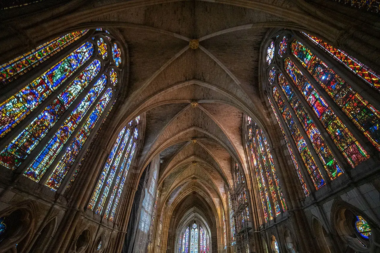 Interior de una catedral con vidrieras de colores y arcos g&oacute;ticos. La luz se filtra a trav&eacute;s de las vidrieras, creando un ambiente m&iacute;stico. Estilo g&oacute;tico.