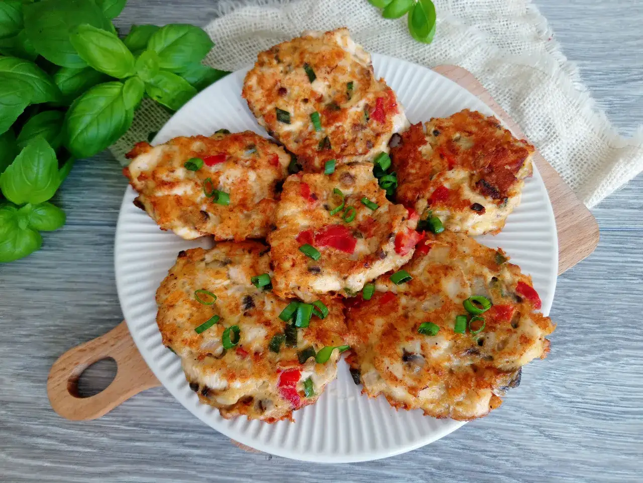 Siekane kotlety z kurczaka z pieczarkami, papryką i szczypiorkiem, podane na białym talerzu.