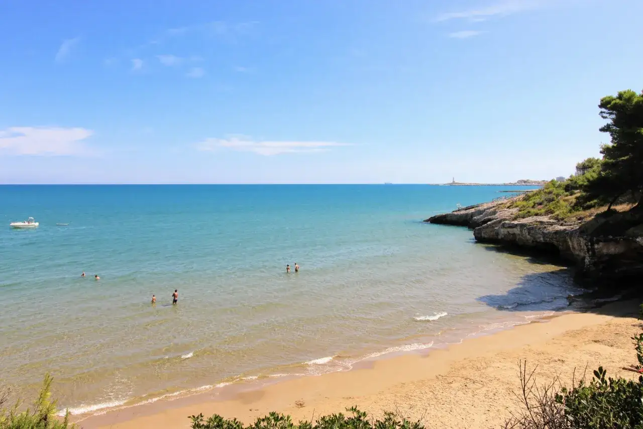 La **spiaggia dei Colombi** &egrave; un angolo di paradiso con sabbia dorata, mare cristallino e scogliere verdi. Alcune persone nuotano e si godono il sole.
