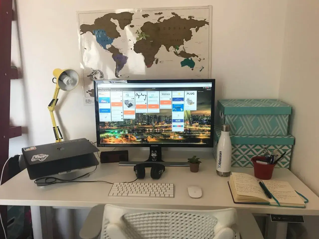 Bureau de télétravail bien organisé avec carte du monde, écran d'ordinateur affichant un tableau Kanban, et fournitures.