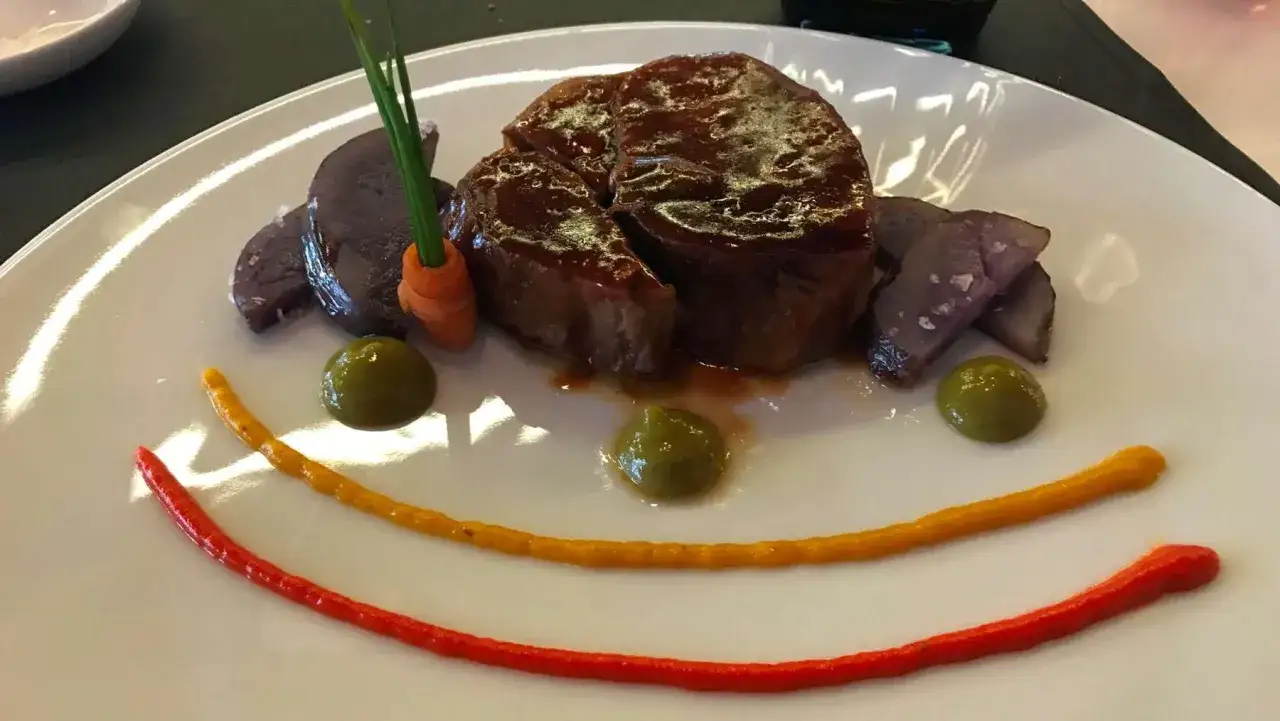 Osobuco de ternera jugoso, acompa&ntilde;ado de patatas moradas, zanahoria y un toque de pur&eacute; de guisantes. &iexcl;Una obra de arte comestible!