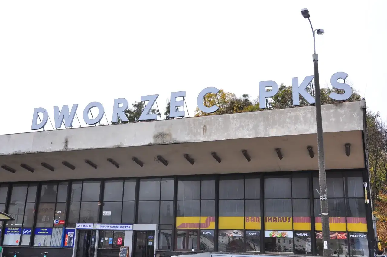Dworzec Autobusowy PKS, skąd odjeżdża autobus nad morze. Widać szyldy sklepów i barów.
