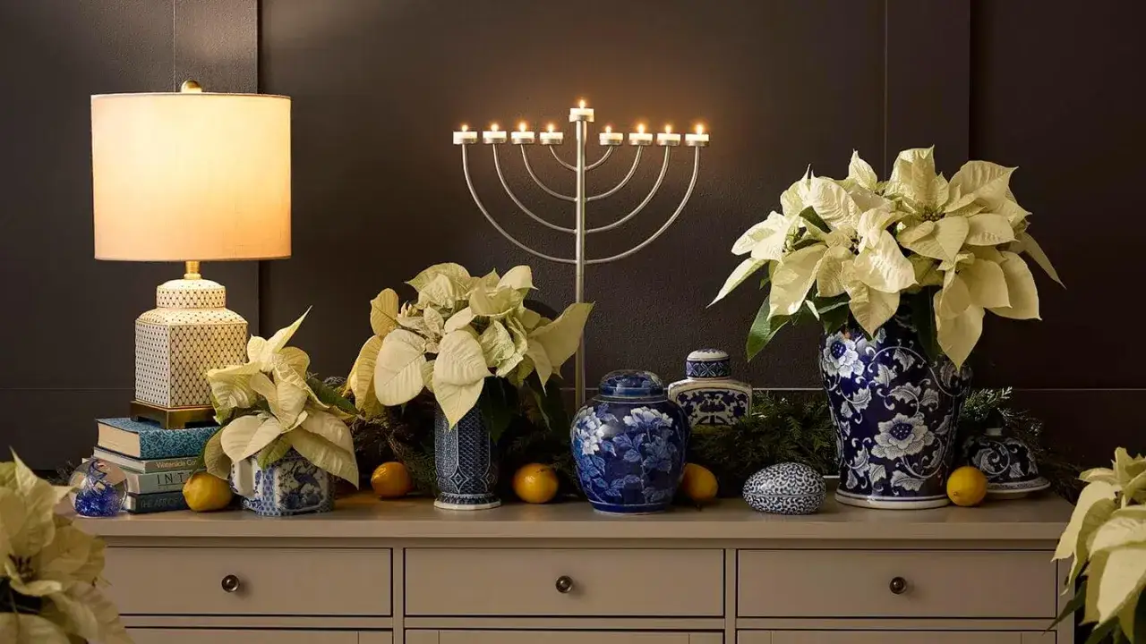 Elegant Chanukah decorating ideas: a silver menorah with lit candles, white poinsettias in blue & white vases, and decorative jars.