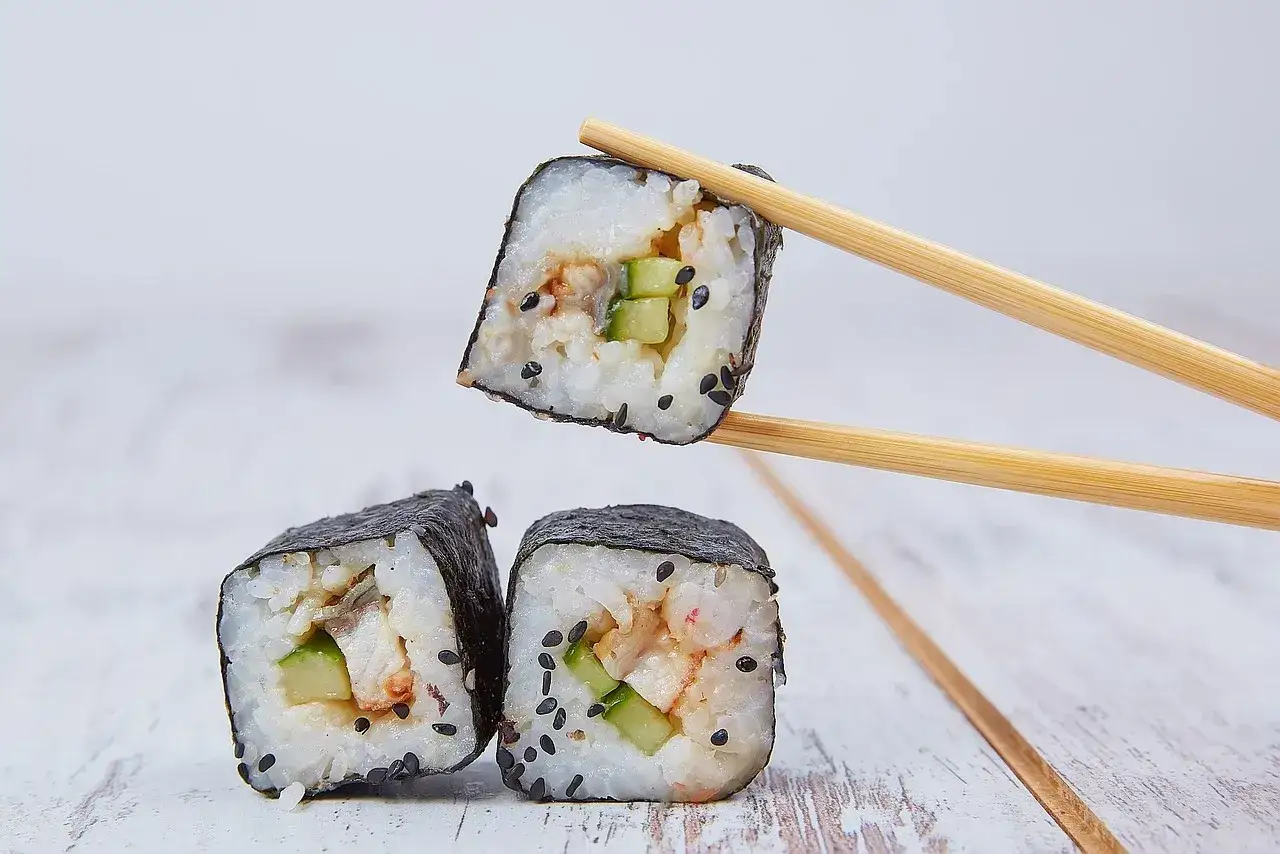 Rolka sushi z og&oacute;rkiem i rybą, podniesiona pałeczkami. Zastanawiasz się, ile octu do sushi?
