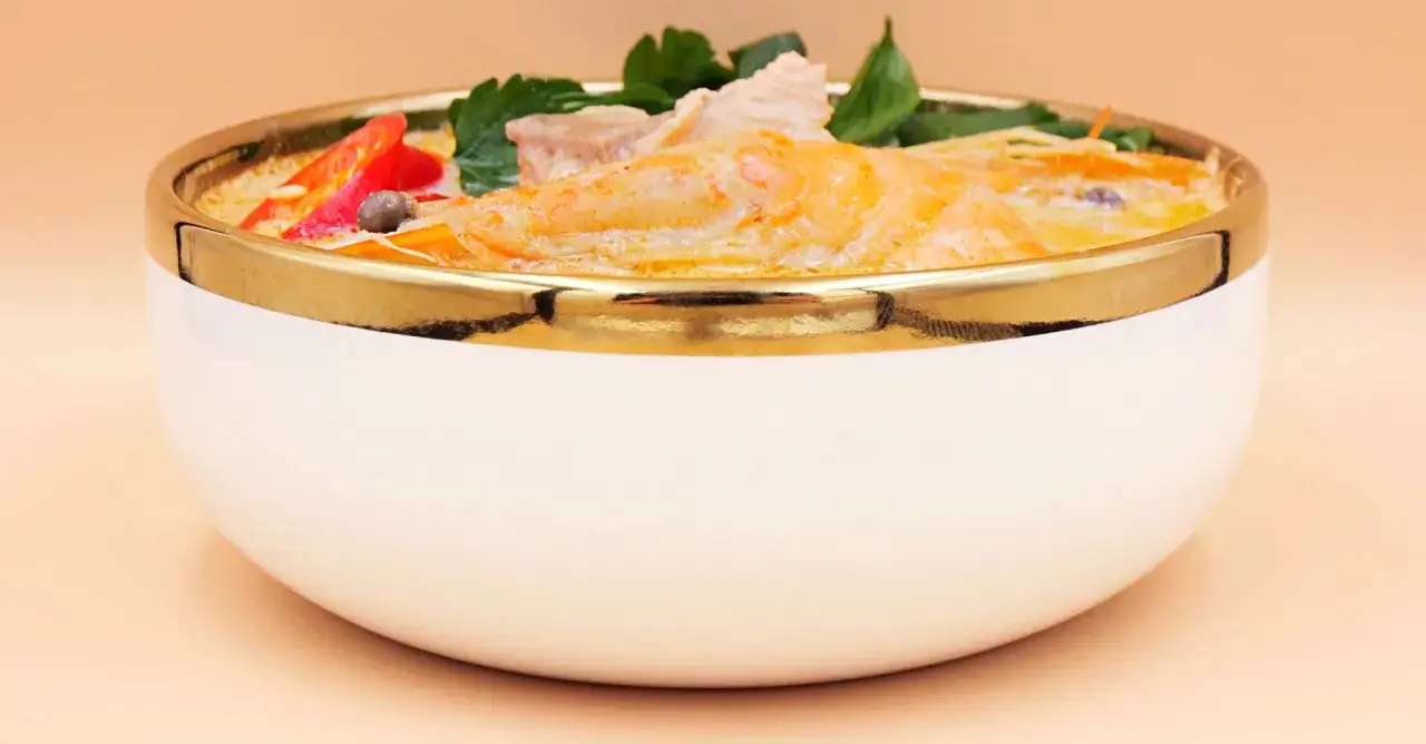 Aksamitny, kremowy sos otula kawałki ryby i krewetki. To aromatyczne ryba po tajsku, podana w eleganckiej misce ze złotym rantem.