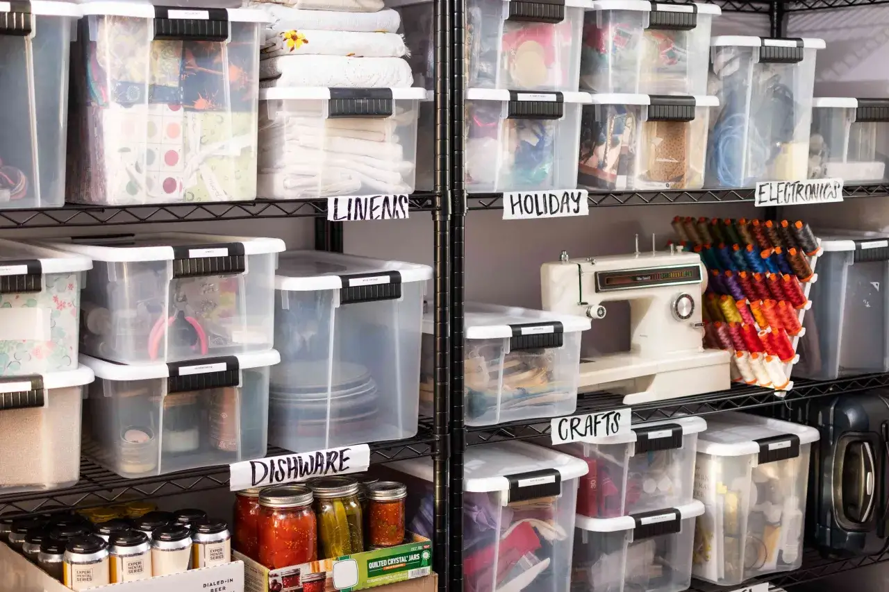 Shelving unit with clear bins for basement storage ideas. Labeled bins hold linens, holiday items, electronics, crafts, and dishware.