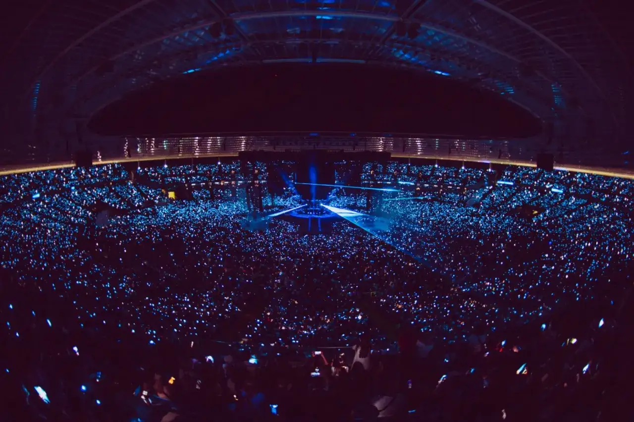 Ogromny stadion wypełniony po brzegi fanami, którzy oświetlają scenę swoimi telefonami podczas koncertu Dawida Podsiadło.