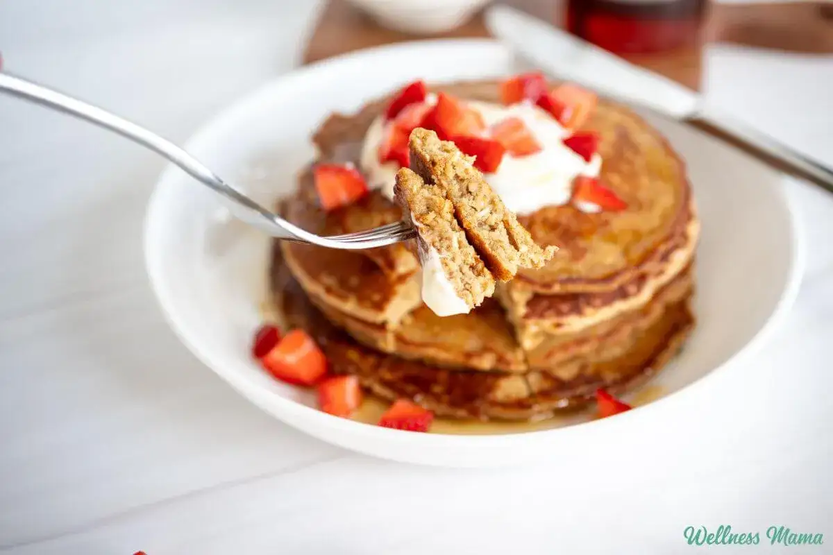 Puszyste fit pancakes z odżywki białkowej, polane syropem i posypane truskawkami. Widok z bliska na widelcu.