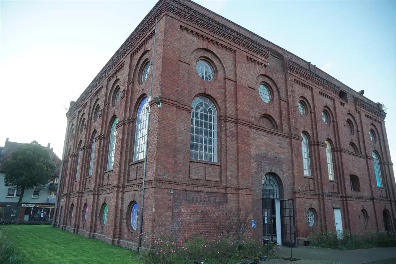 Das imposante Backsteingebäude der Zeche Scherlbeck mit seinen vielen Rundbogenfenstern und kleinen runden Fenstern, die teils bunt beleuchtet sind.