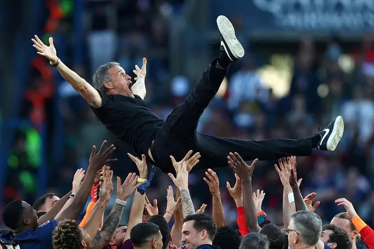 Luis Enrique, kto jest trenerem PSG, uniesiony przez drużynę w geście radości po zwycięstwie.