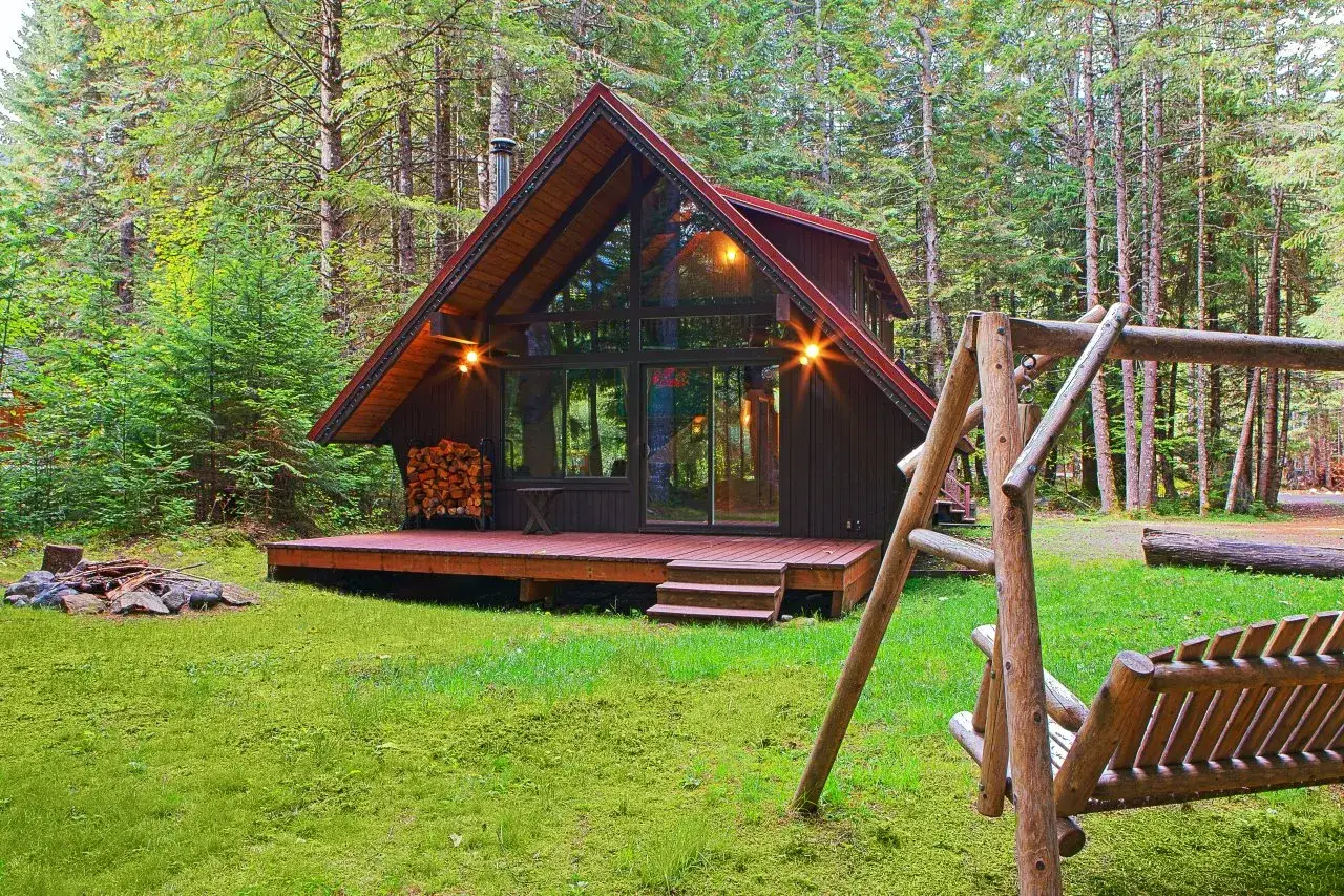 Uroczy domek na odludziu w lesie, z werandą, stosem drewna i drewnianą huśtawką.