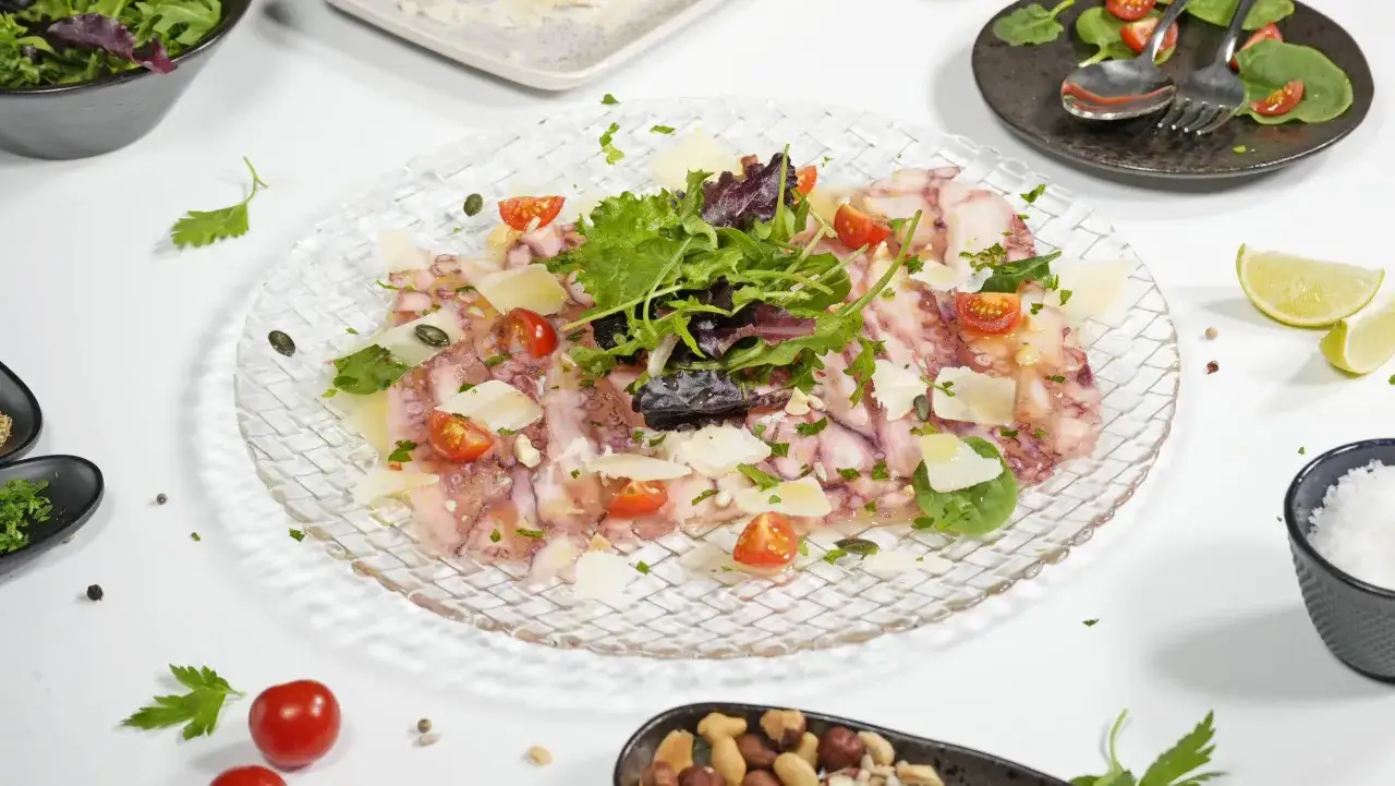 Delicioso carpaccio de pulpo con virutas de parmesano, tomates cherry y hojas verdes frescas.