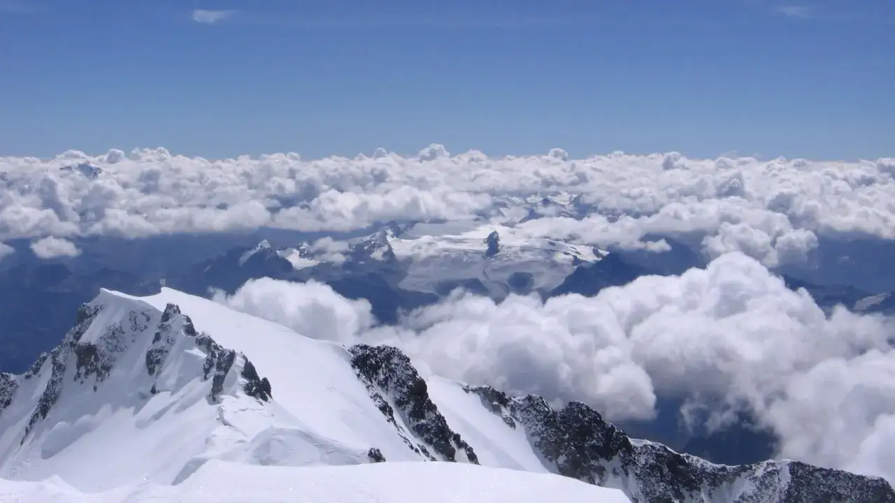 Schneebedeckte Gipfel ragen &uuml;ber Wolken empor. Ein Blick vom Mont Blanc auf eine eisige Berglandschaft.