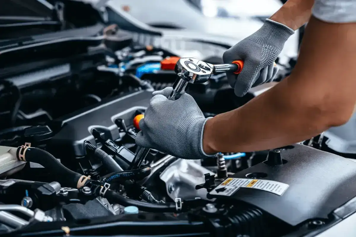 Mechanik w rękawiczkach dokonuje wymiany oleju w samochodzie, używając klucza nasadowego do odkręcenia śruby.