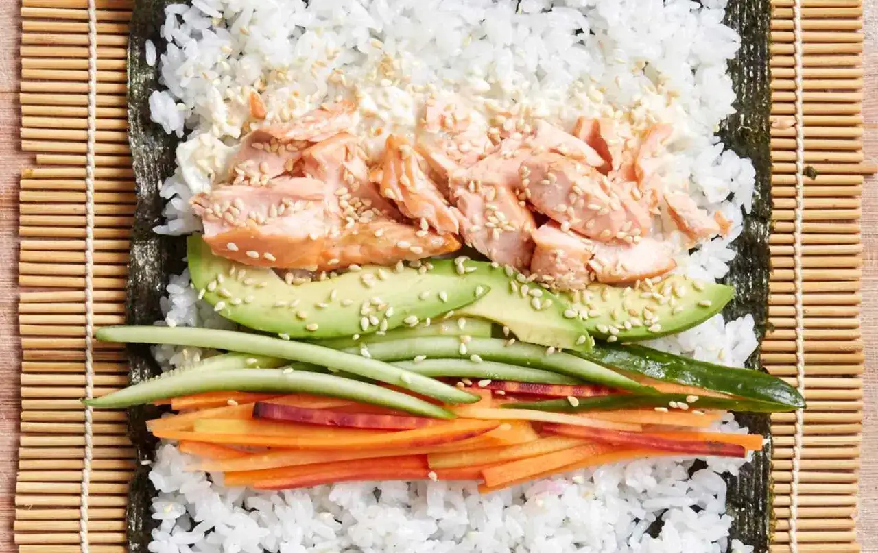 Idealny łosoś do sushi, ułożony na ryżu z awokado, ogórkiem i marchewką, posypany sezamem.