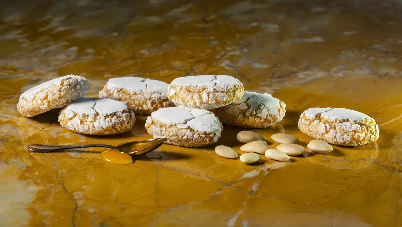 Deliziosi dolci toscani, ricoperti di zucchero a velo, con mandorle e un cucchiaino di miele su un marmo dorato.