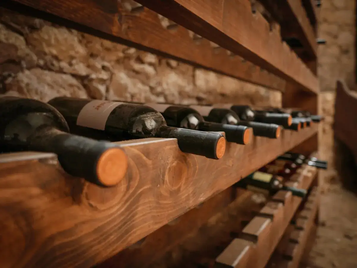 Scaffali in legno con bottiglie di vino disposte in corretta inclinazione, pronte per l'invecchiamento in una cantina rustica.
