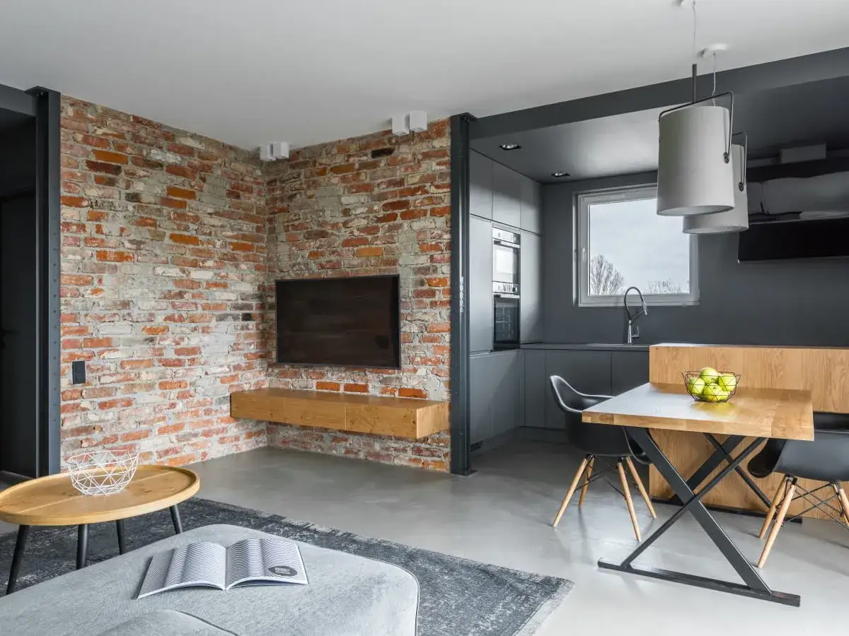 Nowoczesny styl loftowy salon z ceglaną ścianą, betonową podłogą i minimalistyczną kuchnią.
