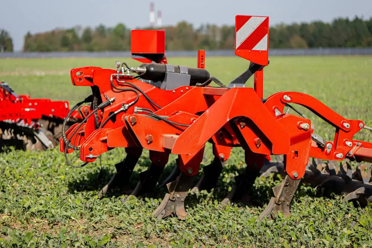 Część pługa z zębami i elementami hydraulicznymi, gotowa do pracy na polu.