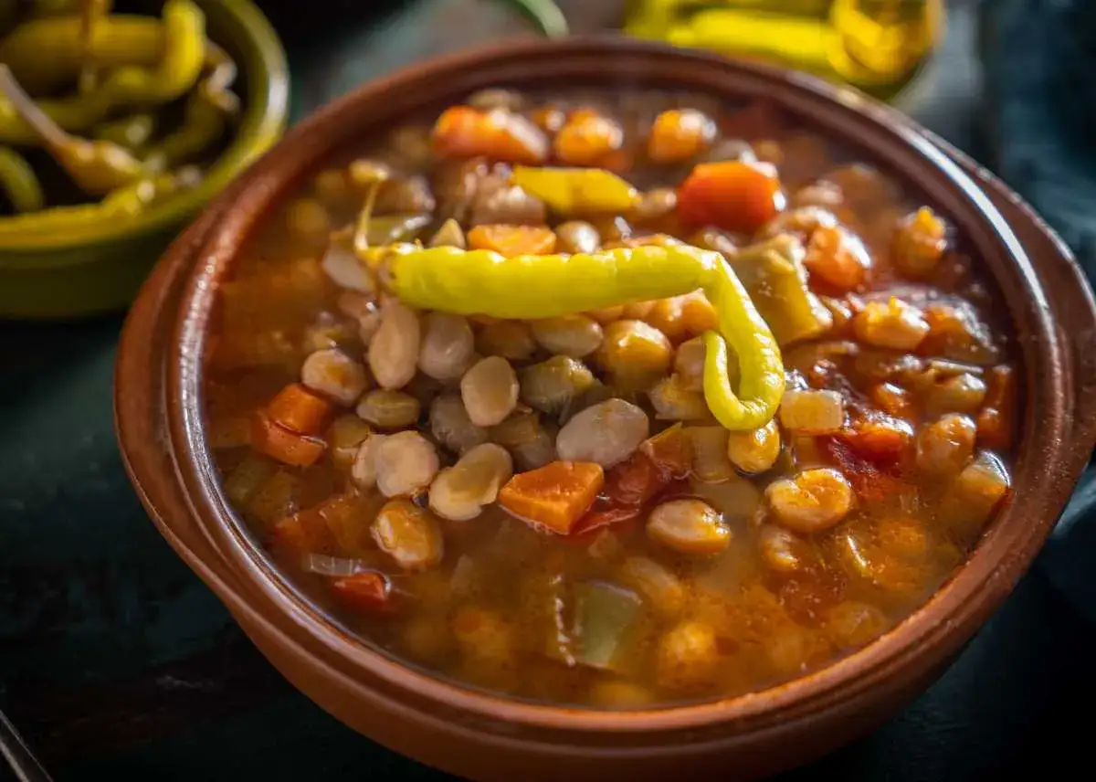 Un cuenco de barro con pochas a la navarra, un guiso reconfortante con judías blancas, zanahoria, pimiento y un chile verde rizado encima.