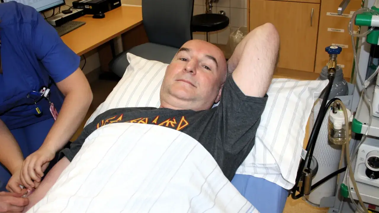 Mann liegt im Bett, bereit für eine Darmspiegelung. Eine Krankenschwester legt eine Infusion. Warum nicht duschen vor Darmspiegelung?