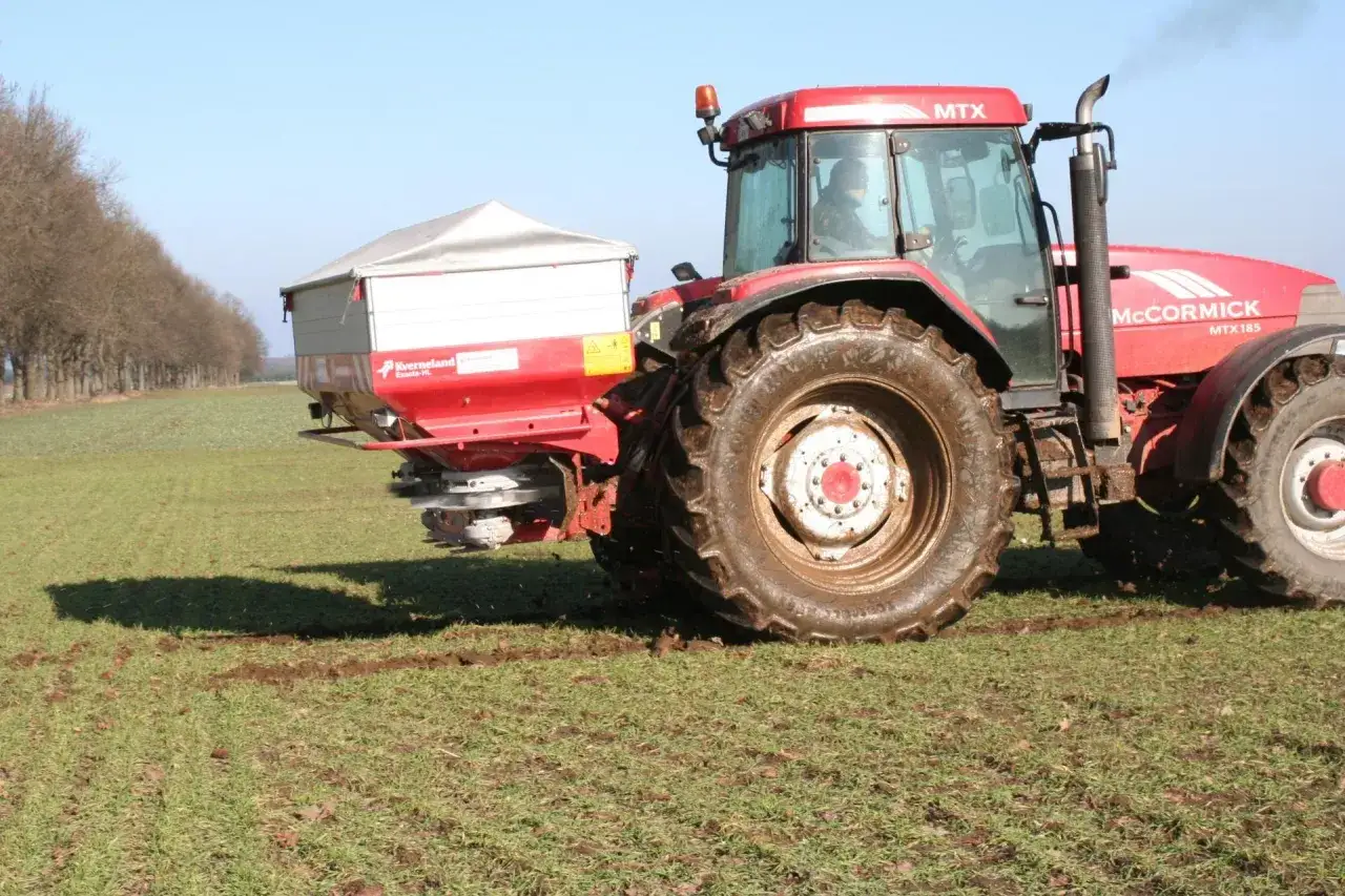 Czerwony traktor McCormick z rozsiewaczem nawozów, pokazujący saletra wapniowa zastosowanie w rolnictwie.