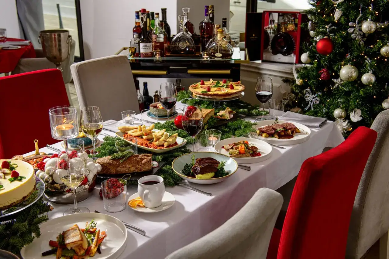 Elegancka wigilia w hotelu: stół zastawiony wykwintnymi daniami, ciastem, winem i ozdobiony choinką.
