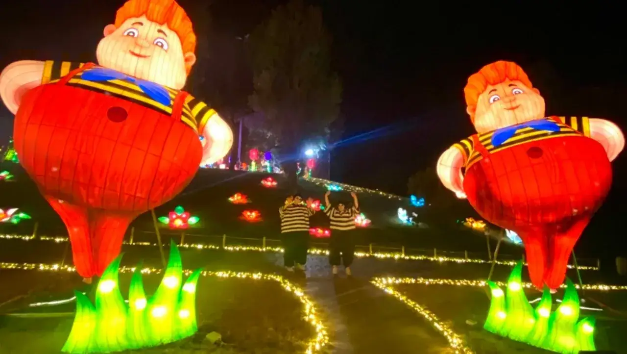 Gigantesche lanterne di un paese delle meraviglie a Rimini, con due persone che ammirano le installazioni luminose.