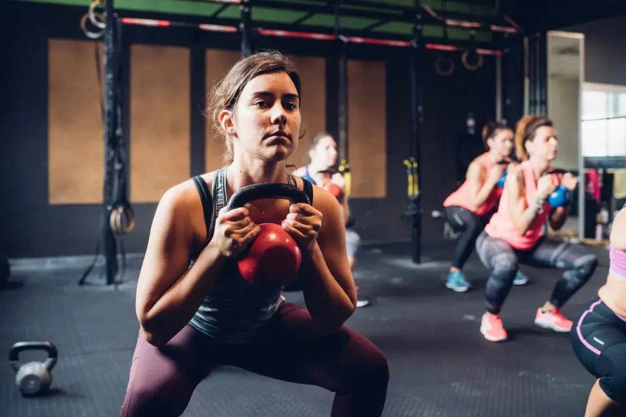 Kvinna tr&auml;nar vikt med kettlebell i gymmet. Flera kvinnor tr&auml;nar i bakgrunden.