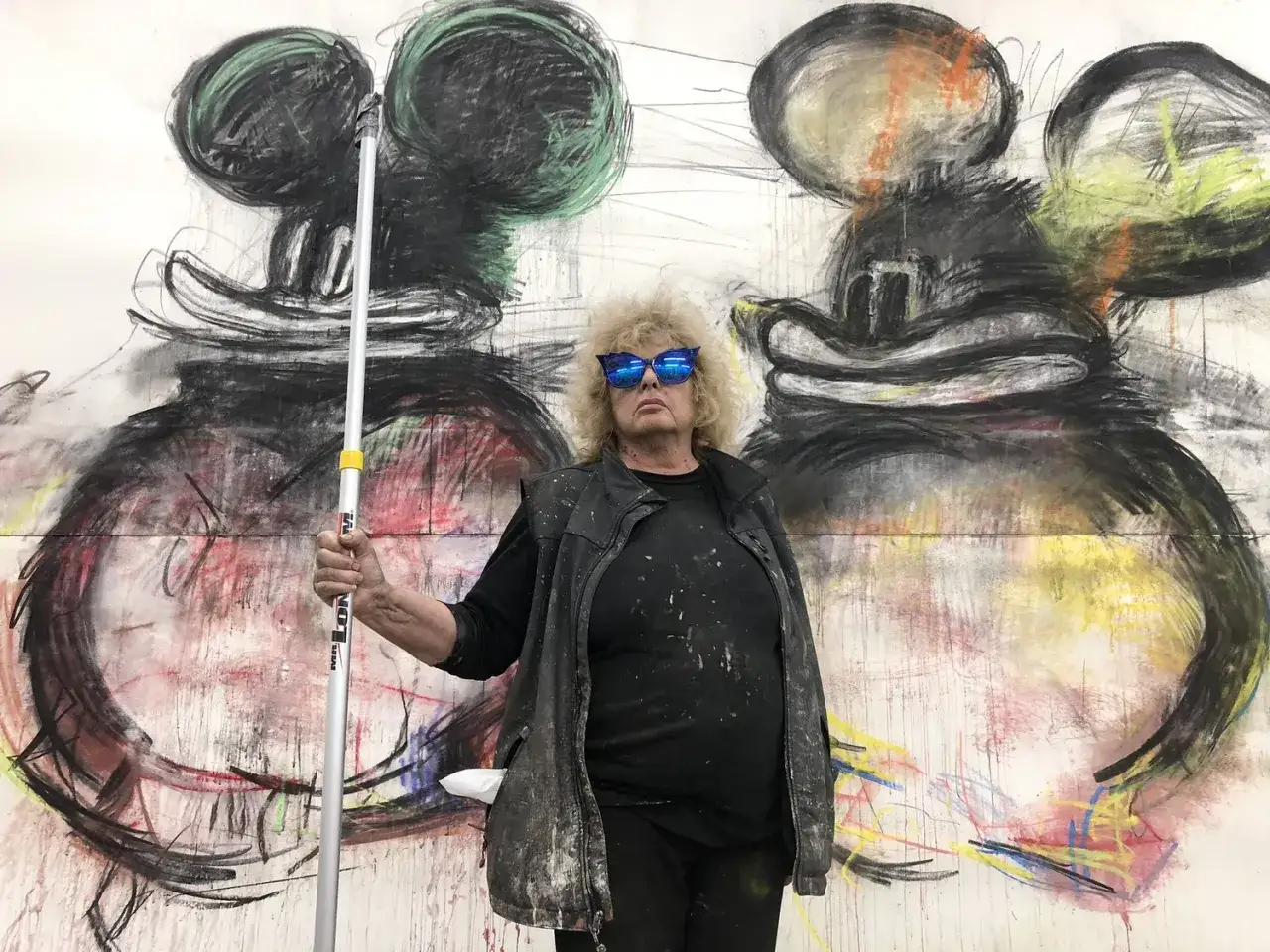 Joyce Pensato stands before her large-scale Mickey Mouse paintings, holding a roller.
