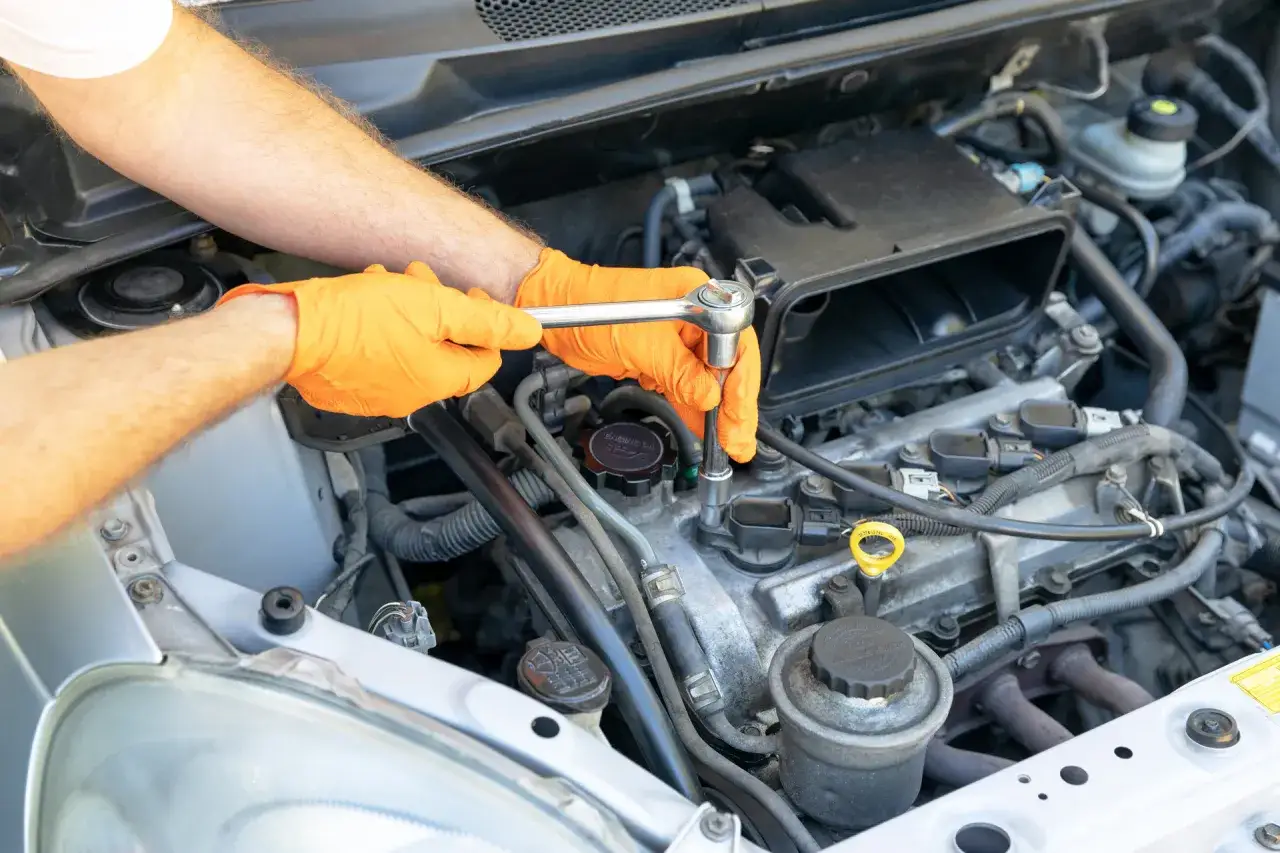 Mains gantées d'orange utilisant une clé pour changer les bougies d'allumage essence d'un moteur de voiture.