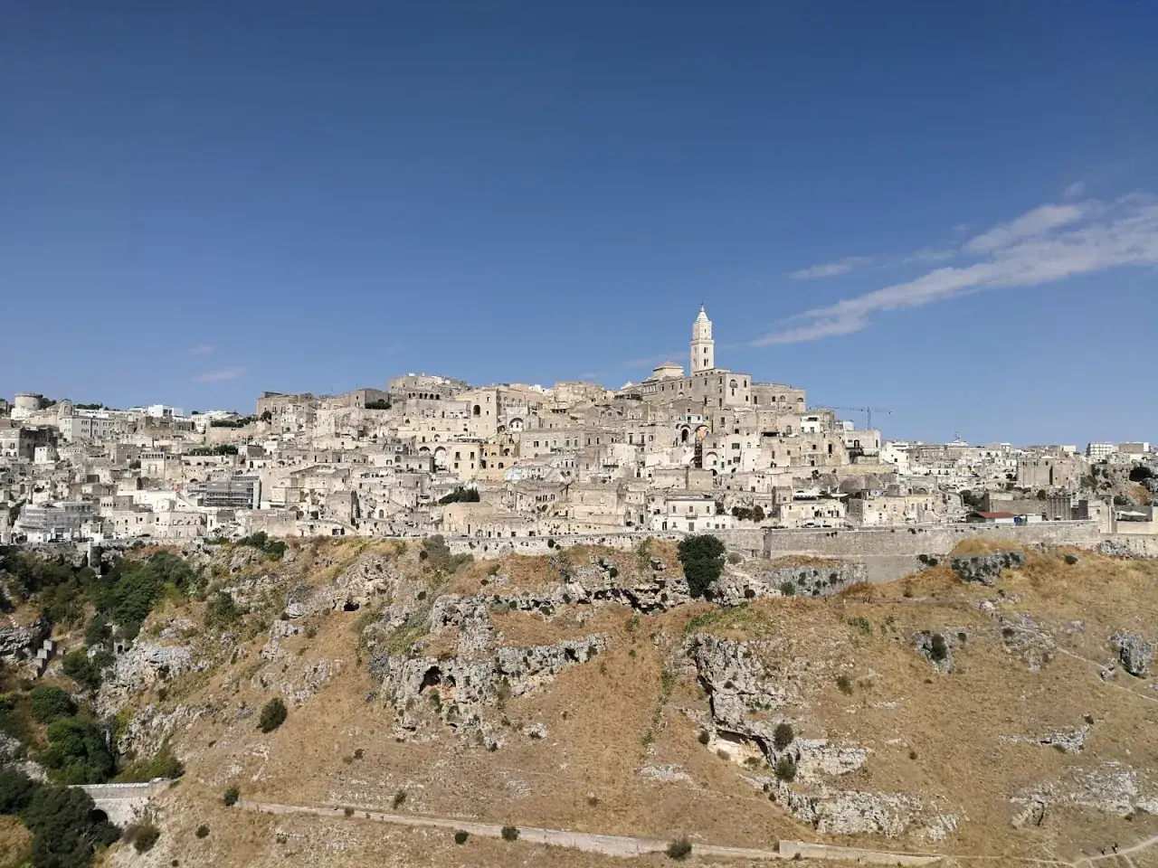 Matera co zobaczyć: starożytne miasto wykute w skale, z białymi domami i wieżą kościelną na tle błękitnego nieba. Widok zapiera dech w piersiach.
