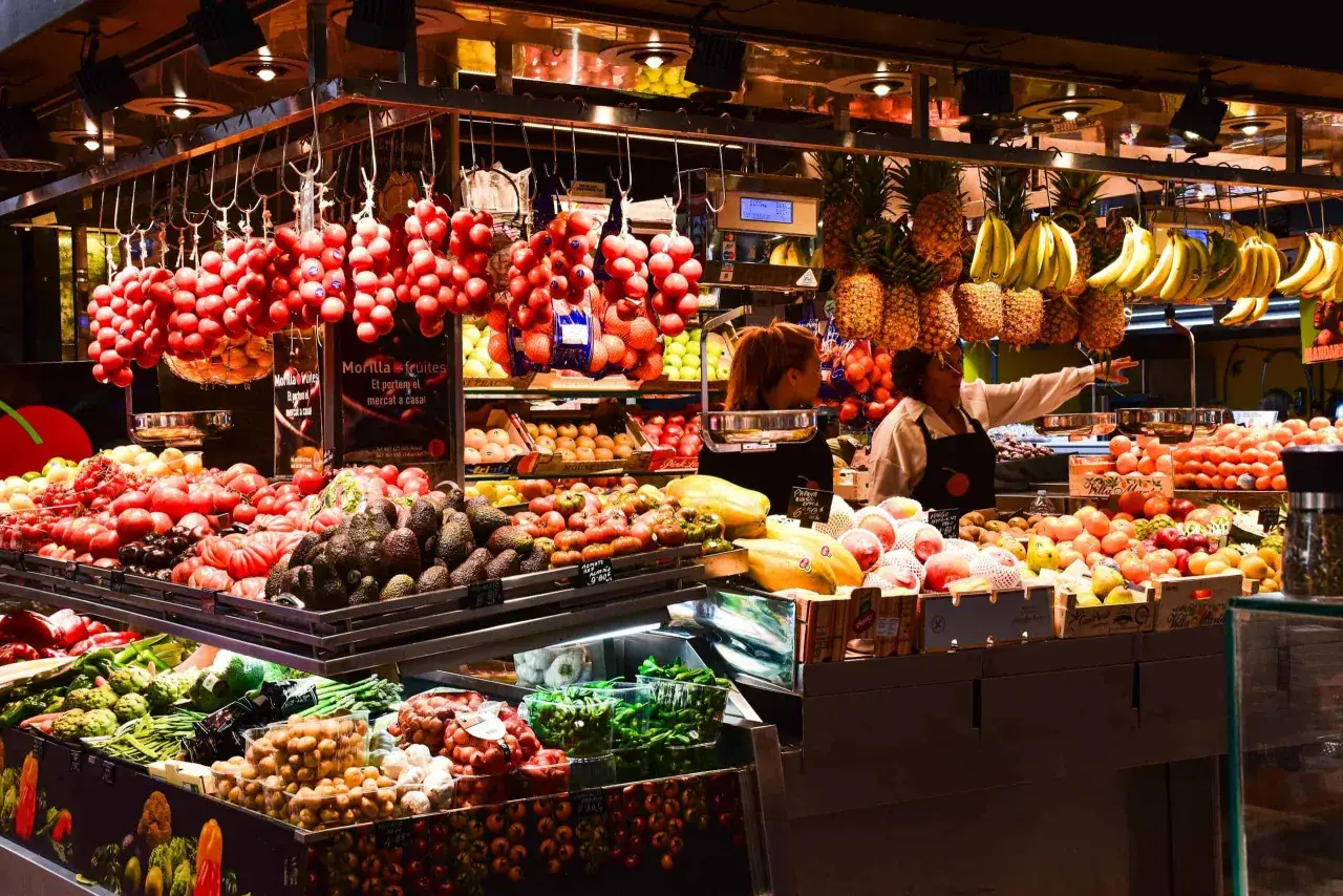 Kolorowe stoisko z owocami i warzywami na Mercat de la Boqueria. Wiszące pomidory, banany, ananasy, awokado i papaje.