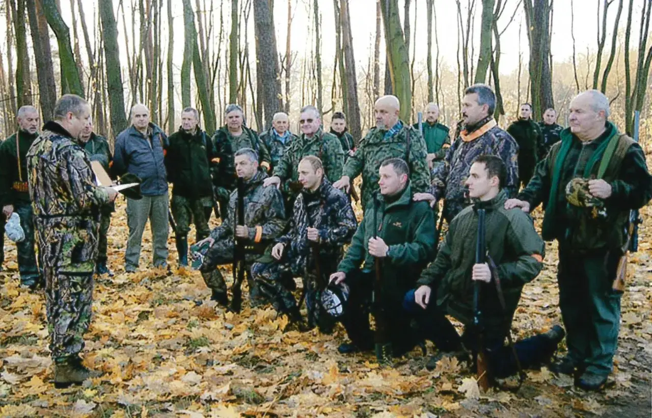 Grupa myśliwych w lesie, wśród nich młody myśliwy, gotowi do polowania.