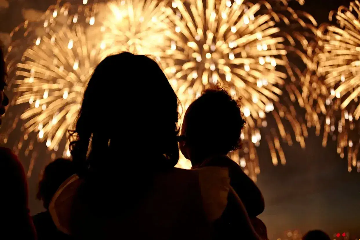 Une mère tient son enfant, admirant un feu d'artifice éclatant. Le **décibel feu d'artifice** résonne dans la nuit.