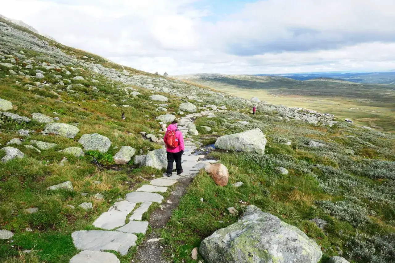 Vandrare med r&ouml;d ryggs&auml;ck p&aring; stenlagd stig i fj&auml;llandskap. En klassisk Fj&auml;llr&auml;ven-upplevelse.