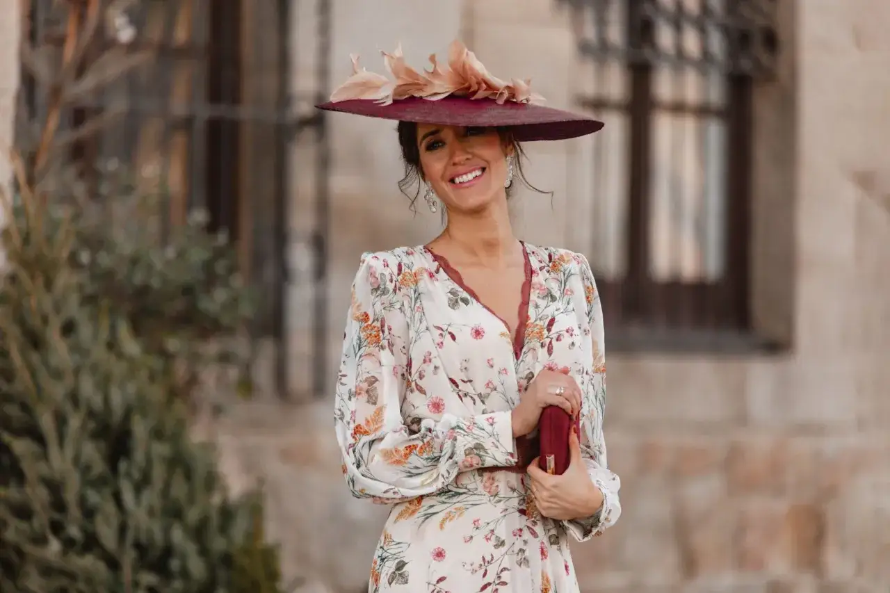 Sonrisa radiante de una invitada en una boda informal campo, con sombrero de ala ancha y vestido floral.