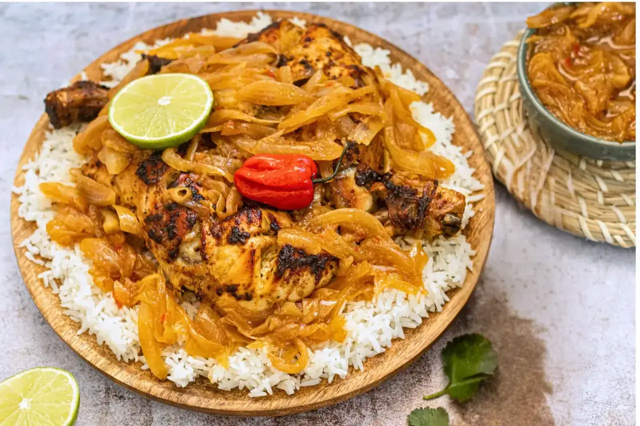 Un plat de poulet yassa savoureux, avec du riz blanc, des oignons caram&eacute;lis&eacute;s, une tranche de citron vert et un piment rouge.