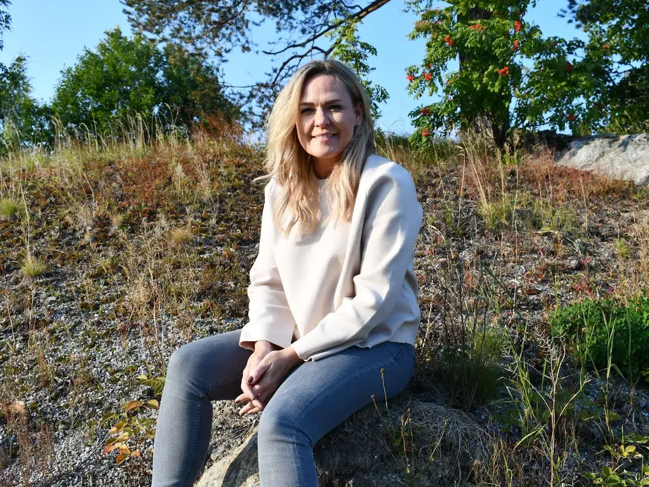 Ulrika Rolfsdotter sitter p&aring; en sten utomhus, omgiven av gr&auml;s och tr&auml;d.