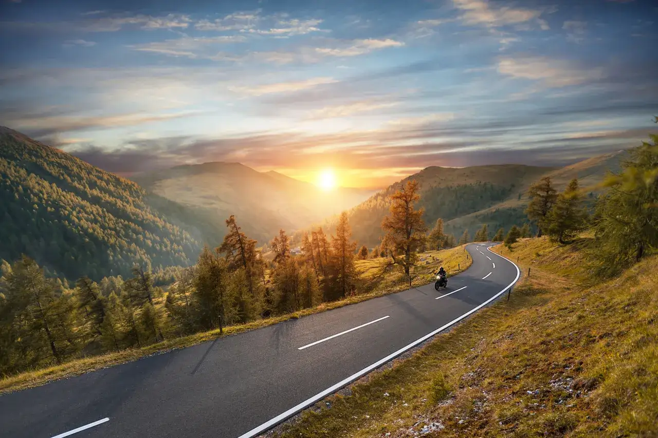 Un motociclista percorre una strada tortuosa tra montagne boscose al tramonto. Questo &egrave; il vero significato di 